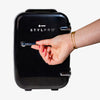 Eine Hand mit roten Nägeln öffnet einen schwarzen Beauty Fridge vor weißem Hintergrund.
