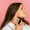 Eine Frau, die vor einem rosa Hintergrund den Fabulous Firmer Neck & Face Smoother auf ihrem Kinn verwendet.