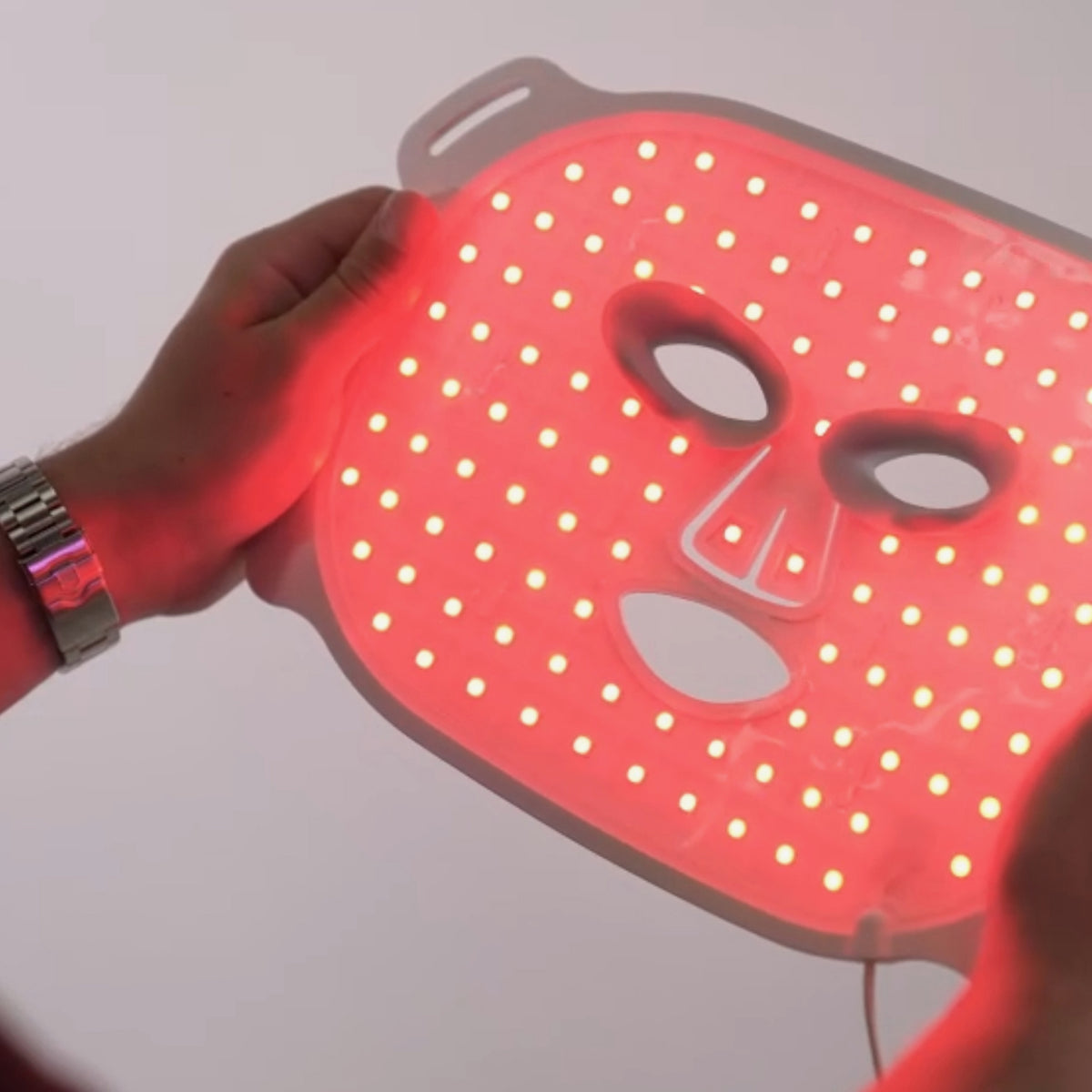 Person hält die durchleuchtete STYLPRO LED-Gesichtsmaske mit rot leuchtenden LEDs, die gleichmäßig über die Maske verteilt sind.