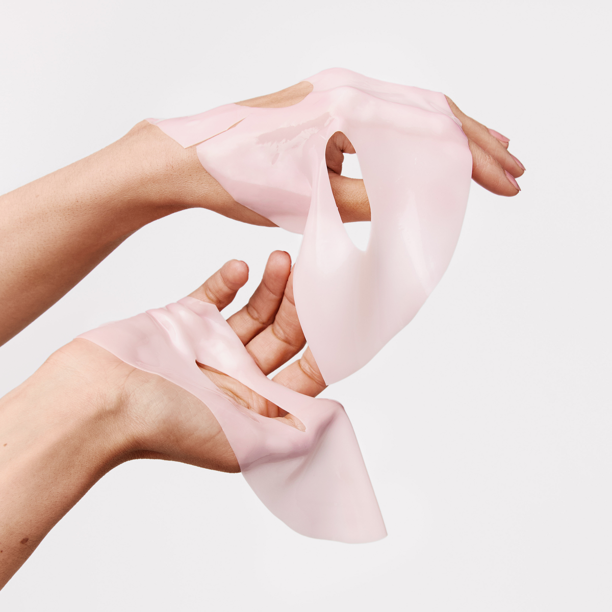 Zwei Hände halten die XLASH Collagen Hydrogel Hyal-Maske – ein rosa Blatt mit Ausschnitten – vor einem schlichten weißen Hintergrund.