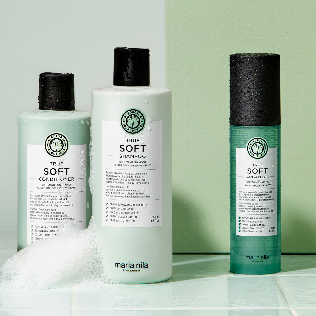 Drei Produkte der Maria Nila True Soft Reihe mit Wassertropfen und Schaum auf mintgrünem Hintergrund.