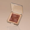 Offenes Kompaktetui mit strukturiertem braunem Skin Bronzing-Puder mit der Prägung „NABLA“, abgebildet auf beigem Hintergrund.