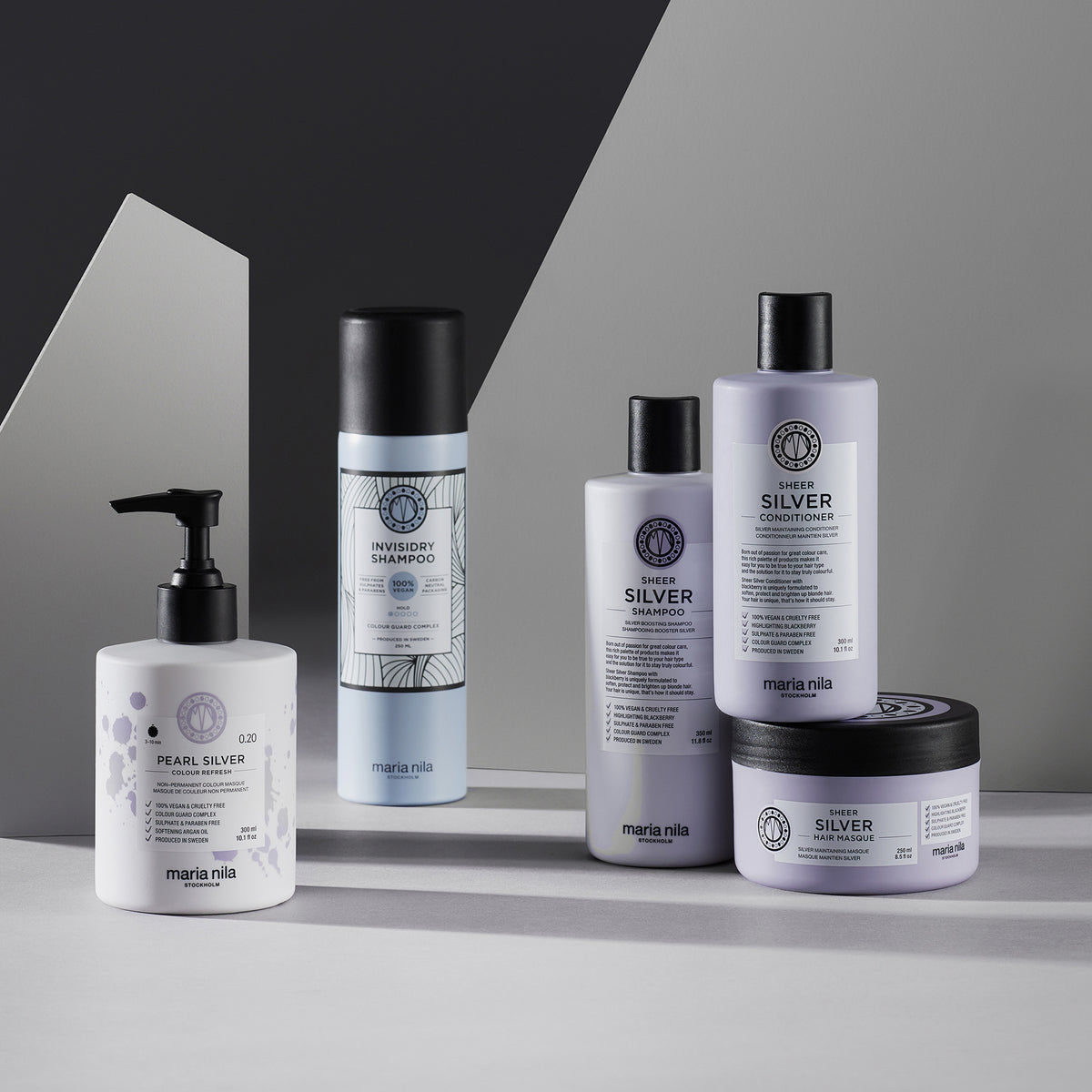 Maria Nila Invisidry Shampoo und weitere Haarpflegeprodukte, dargestellt auf einer grauen und weißen Fläche mit geometrischem Hintergrund.