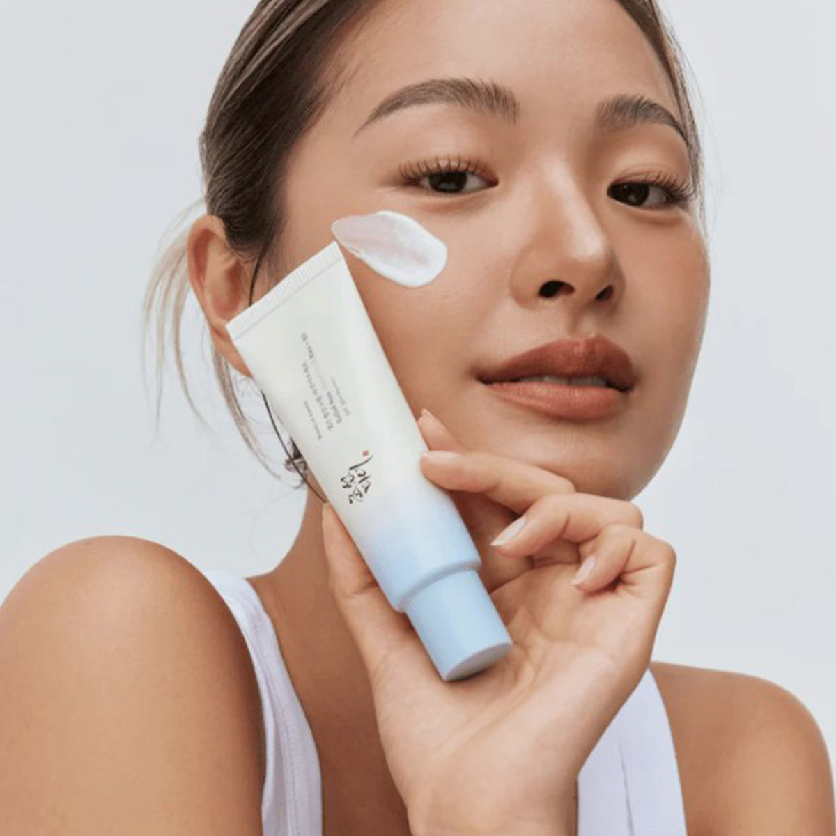 Eine Person hält Relief Sun Aqua Fresh Rice + B5 SPF 50+ an ihr Gesicht und dabei einen Klecks Creme auf der Wange