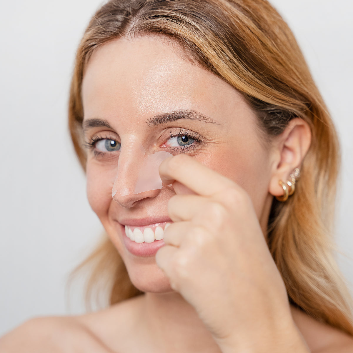 Eine Frau lächelt, während sie Zitproof Nose Strip auf ihre Nase klebt