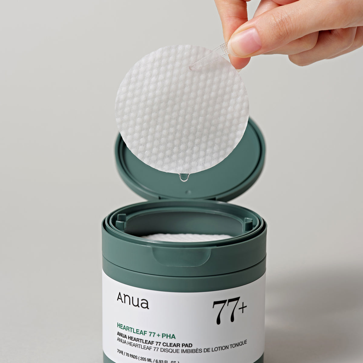 Eine Hand hält ein rundes strukturiertes Pad über einem offenen Tiegel Heartleaf 77 % Toner Pad.