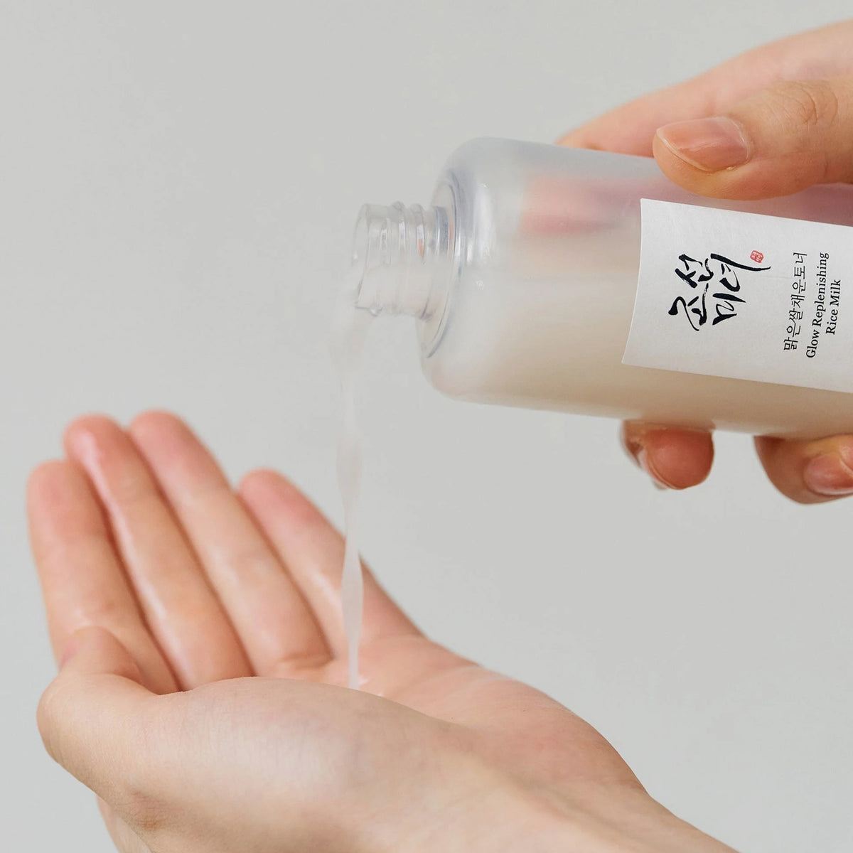 Eine Hand gießt die Glow Repleneshing Rice Milk in die andere Handfläche.