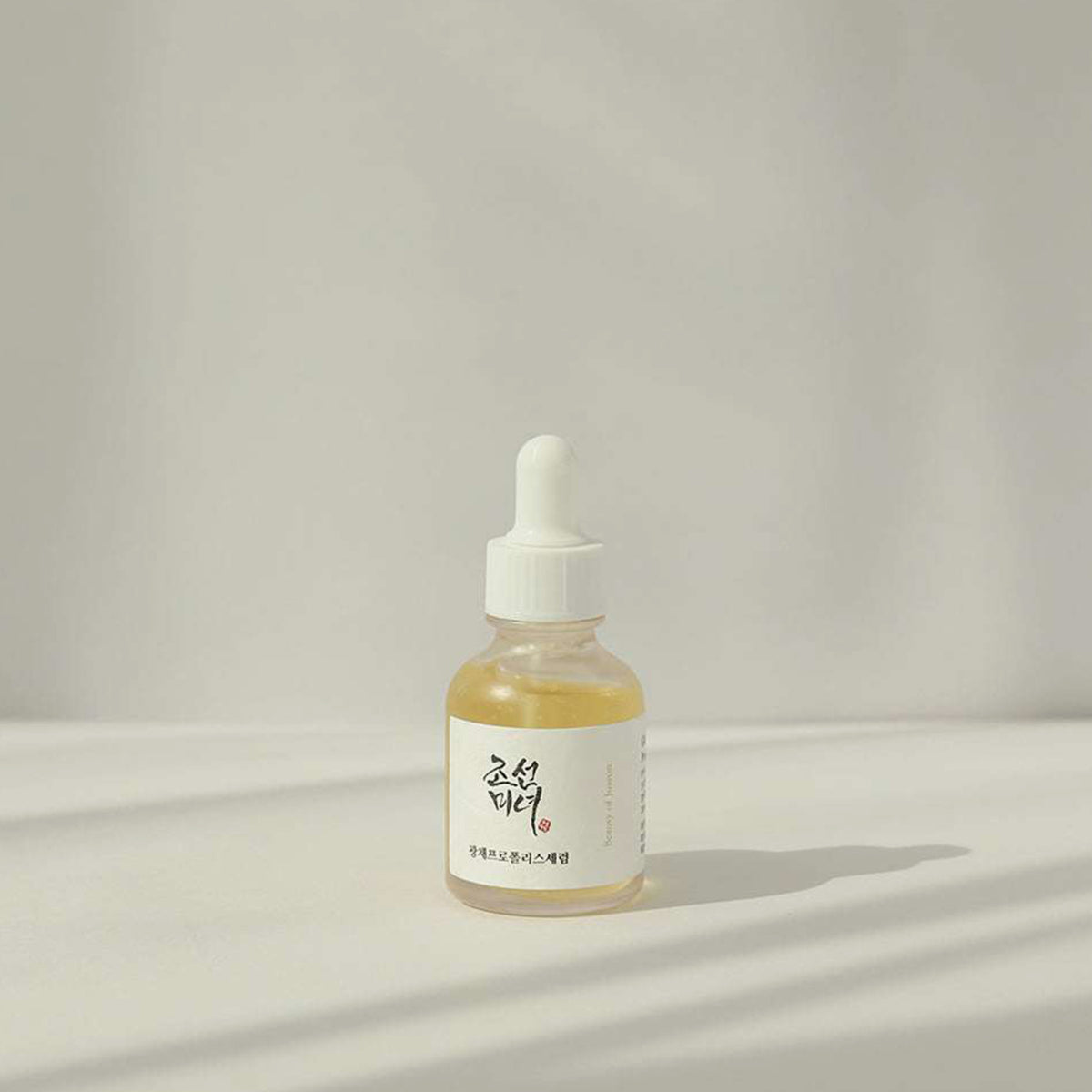 Eine Flasche Glow Serum: Propolis+Niacinamide steht auf einer weißen Oberfläche mit leichten Schatten