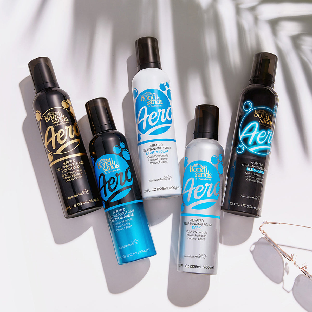 Fünf Flaschen Aero One Hour Express Self Tanning Foam sind auf einer weißen Oberfläche mit Sonnenbrille platziert