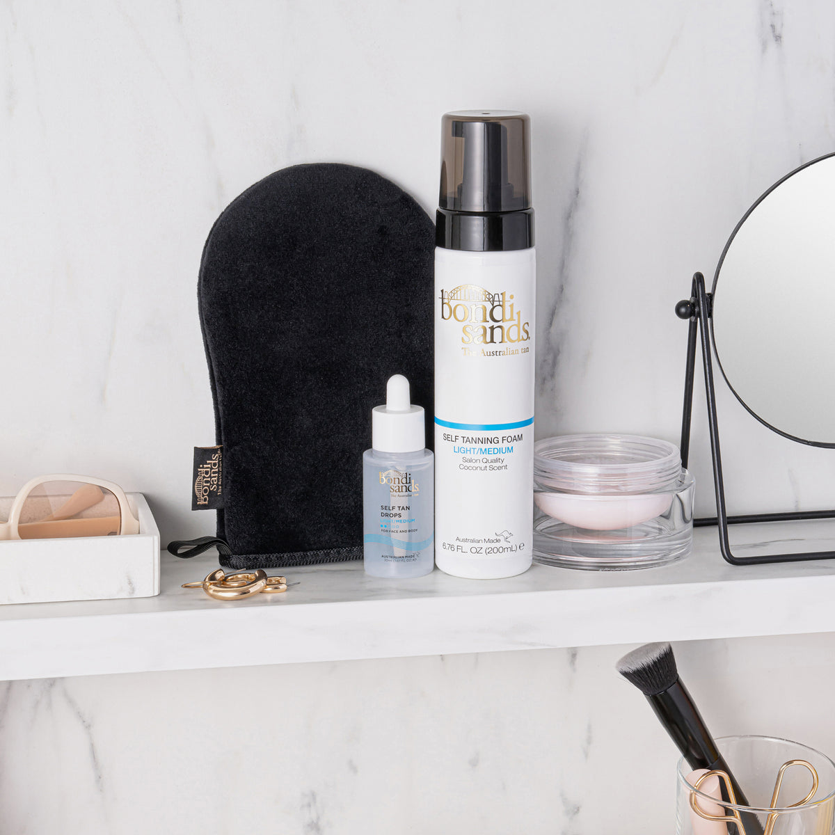 Bondi Sands Application Mitt, Self Tanning Mousse & Self Tan Drops neben Kosmetika auf einem weißen Regal