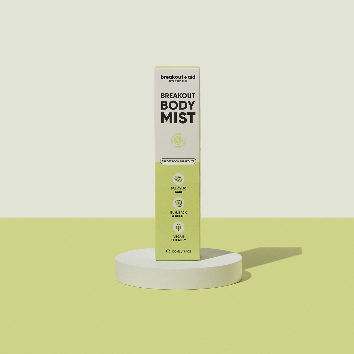 Hohe, rechteckige Breakout+Aid Breakout Body Mist-Flasche auf einem runden Sockel, beschriftet mit den Angaben Salicylsäure, Anwendungsbereiche und vegan.