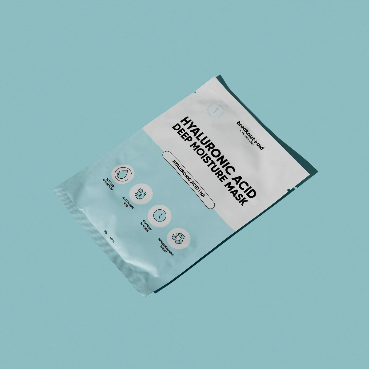 Eine Breakout+Aid-Feuchtigkeitsmaske mit Hyaluronsäure in einer Einzelpackung, versehen mit Text und Symbolen zu den Themen Feuchtigkeitsversorgung und biologische Abbaubarkeit.