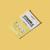 Eine gelbe, rechteckige Breakout+Aid-Vitamin-C-Maskenverpackung mit Symbolen, die Vitamin C, Hyaluronsäure und Süßholzwurzelextrakt darstellen.