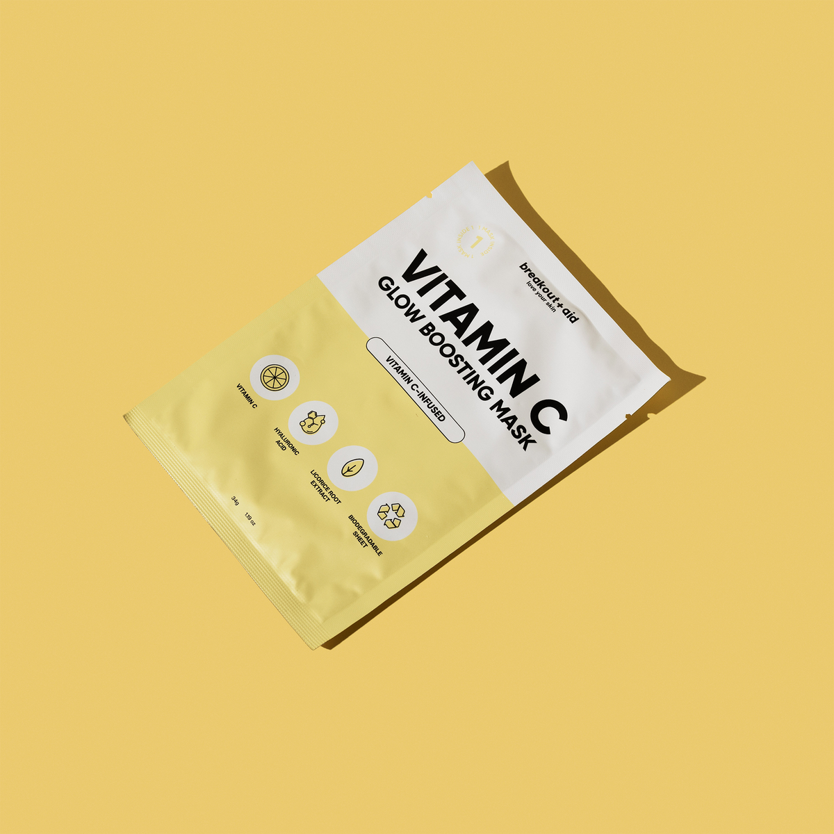Eine gelbe, rechteckige Breakout+Aid-Vitamin-C-Maskenverpackung mit Symbolen, die Vitamin C, Hyaluronsäure und Süßholzwurzelextrakt darstellen.