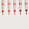 Fünf Catrice Colour Cushion Juicy Lip Oils nebeneinander, aus jedem Applikator tropft glänzendes farbiges Lip Oil in unterschiedlichen Nuancen.