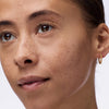 Nahaufnahme einer Frau mit braunen Augen die den Instant Bright Serum Concealer 018C auf der Haut präsentiert.