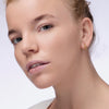 Nahaufnahme einer Person mit blondem Haar und hellblauen Augen die den Instant Bright Serum Concealer 020W auf der Haut präsentiert.
