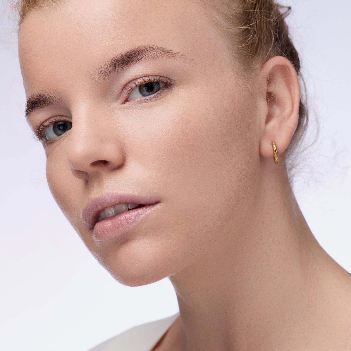 Nahaufnahme einer Person mit blondem Haar und hellblauen Augen die den Instant Bright Serum Concealer 020W auf der Haut präsentiert.