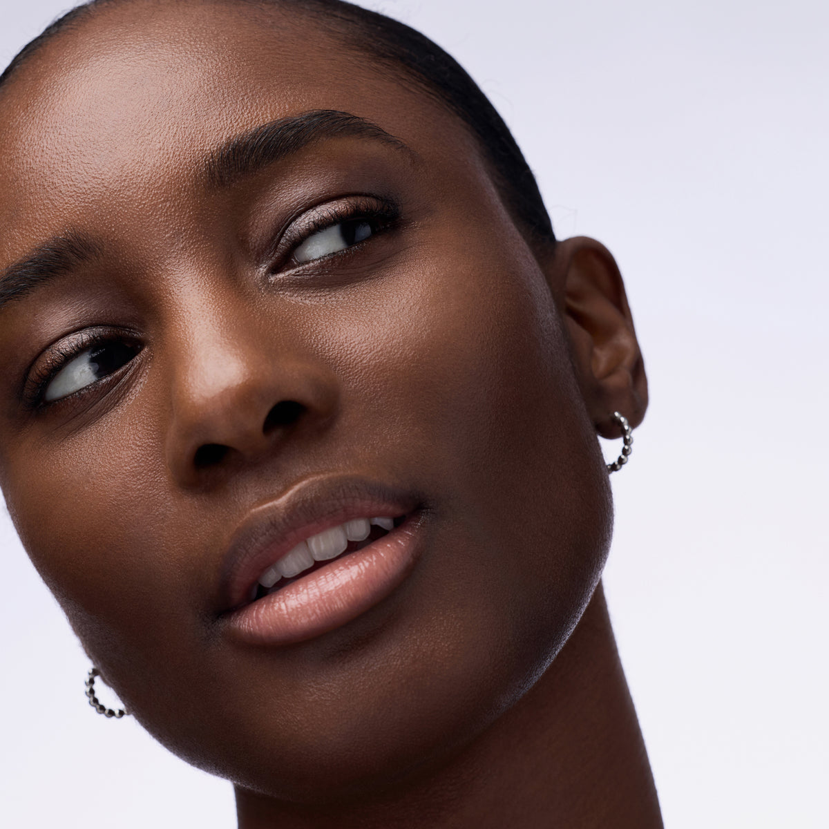 Nahaufnahme einer Person mit schwarzem Haar und dunklem Teint, die den Instant Bright Serum Concealer 090C auf der Haut präsentiert.
