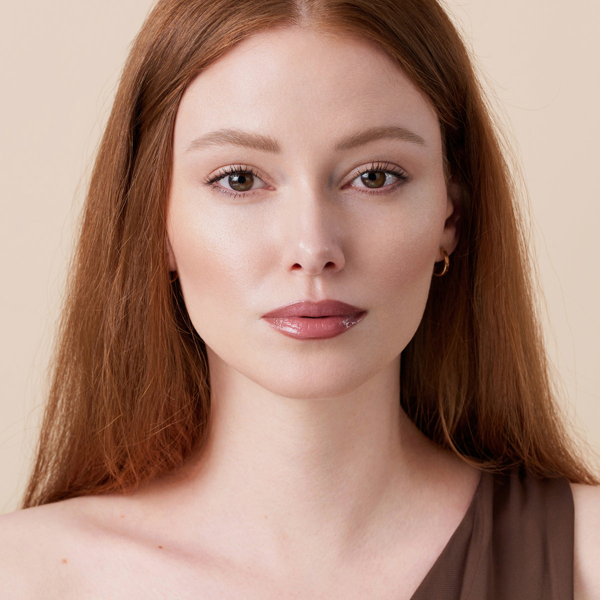 Eine Frau mit rotbraunem Haar blickt in die Kamera, während sie Soft Glam Filter Fluid präsentiert.