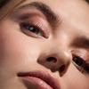 Nahaufnahme des Gesichts einer Frau mit schimmerndem rosa Lidschatten aus der Wonder Woman-Lidschattenpalette, Mascara und glänzenden Lippen.