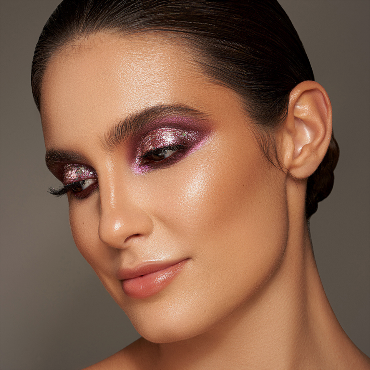 Eine Frau mit zurückgekämmtem Haar, strahlender Haut und nudefarbenem Lippenstift präsentiert ein glitzerndes lilafarbenes Augen-Make-up, das mit Danessa Myricks Beauty Infinite Chrome Flakes Sweet Tooth kreiert wurde.