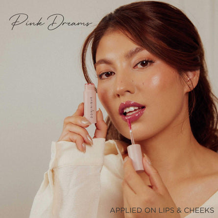 Eine Frau trägt Pillow Soft Hydrating Lip & Cheek Stain in Pink mit einem Applikator auf; der Text lautet „Pink Dreams“ und wird auf Lippen und Wangen aufgetragen.