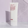 Eine Tube Liquid Rollers Curl Balm steht auf einer hellen Oberfläche mit einem sanften violetten Hintergrund.