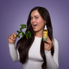 Eine Frau mit langen dunklen Haaren hält einen Minzzweig und eine Flasche Hair Syrup's Mint Condition vor einem lila Hintergrund.
