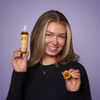 Eine lächelnde Frau, die in der einen Hand eine Flasche Hair Syrup The Original und in der anderen Hand eine Aprikose hält.