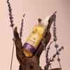 Eine Flasche Hair Syrup's Zen ruht auf einem Stück Holz, umgeben von Lavendelzweigen.