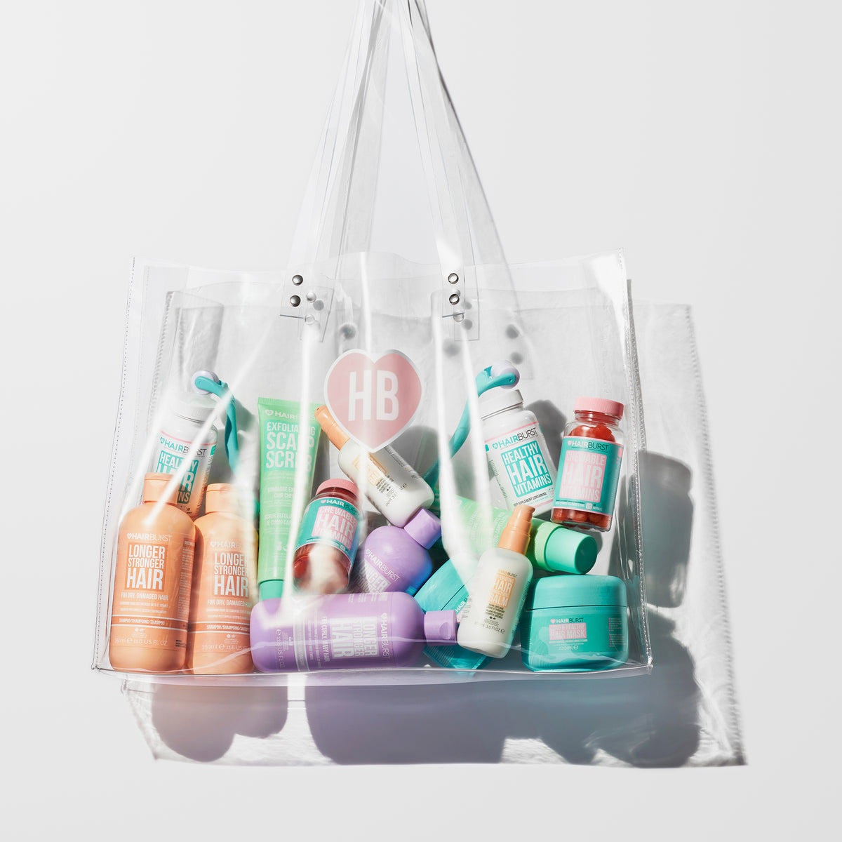 Durchsichtige Tragetasche gefüllt mit farbenfrohen Hairburst-Produkten vor einem hellrosa Hintergrund.