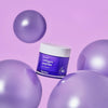 Ein Tiegel Collagen Peptide Eye Cream zwischen glänzenden violetten Kugeln vor einem lila Hintergrund.