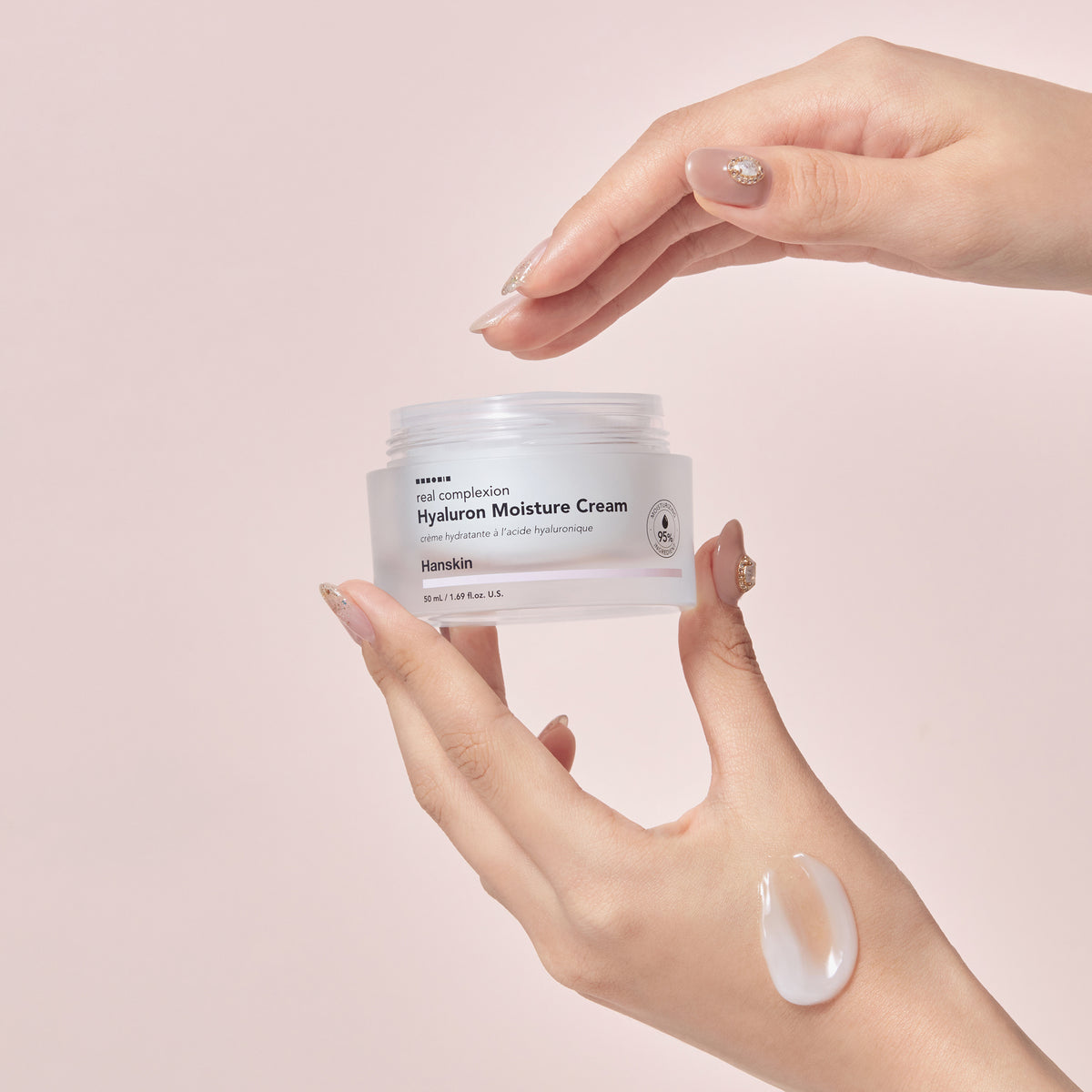 Eine Hand hält einen Tiegel mit der Real Complexion Hyaluron Moisture Cream,vor einem rosa Hintergrund.