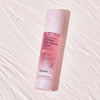 Eine rosa Flasche Real Complexion Hyaluron Pink Capsule Serum, präsentiert auf einer strukturierten weißen Oberfläche.