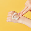 Eine Hand trägt den Pore Cleansing Balm PHA auf den Handrücken der Anderen vor gelbem Hintergrund.