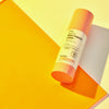 Vor einem gelb-orangen Hintergrund ist eine Flasche Vitamin C Glow Capsule Lotion zu sehen.