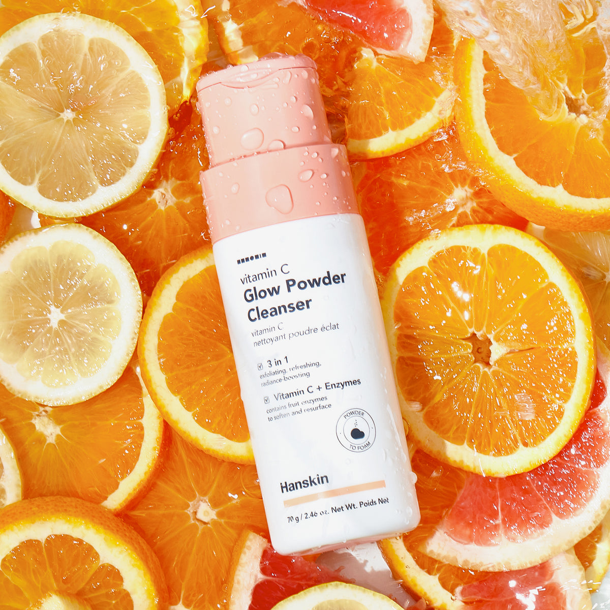 Eine Flasche Vitamin C Glow Powder Cleanser schwebt im Wasser, umgeben von Orangen-, Zitronen- und Grapefruitscheiben.