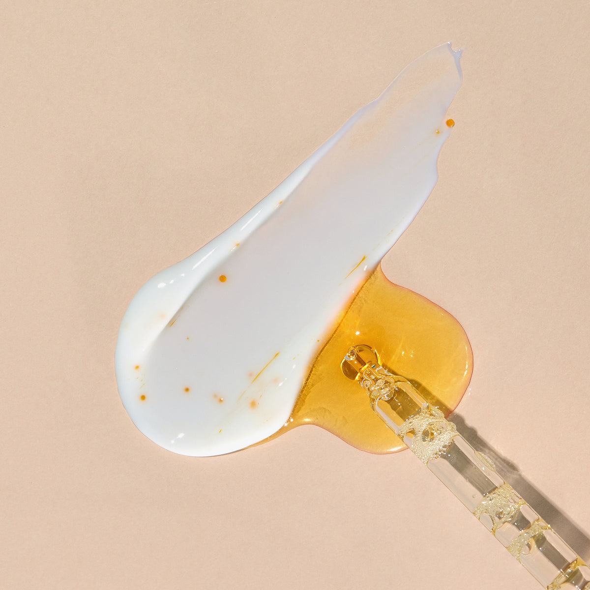Eine Pipette mit Vitamin C Glow Serum und ein Klecks weißer Creme vermischen sich auf einem beigen Hintergrund.