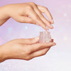 Hände nehmen etwas Fix Potion-Gel aus einem transparenten tiegel, vor einem zartrosa, glitzernden Hintergrund.