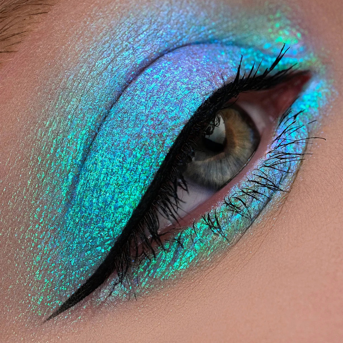 Nahaufnahme eines Auges mit dramatischem Eyeliner und türkis schimmerndem Opal Moonstone Loose Multichrome Eyeshadow in Clever Clugs.