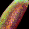 Nahaufnahme einer Fingerspitze, die in den Opal Moonstone Loose Multichrome Eyeshadow Sassy Pants getaucht wurde und gelb-grün und rosa-bronze glitzert.