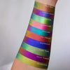 Ein Unterarm mit mehreren bunten metallisch schimmernden Farbmustern des Original Multichrome Loose Eyeshadow.