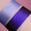 Zwei schimmernde Muster des Pastel Duochromes Loose Eyeshadow Frosting mit unterschiedlichen Grundierungen; eins mit der Black Base (dunkellila), eins mit der Fix Potion (hellviolett).