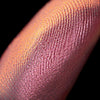 Nahaufnahme einer Fingerspitze, die in den Pastel Duochromes Loose Eyeshadow Pigtails getaucht wurde und pfrisich und rosé glitzert.