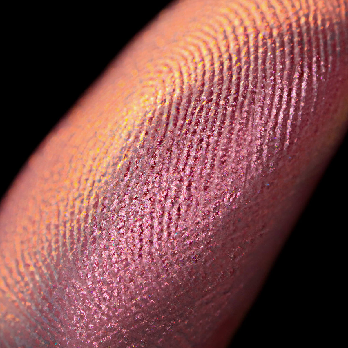 Nahaufnahme einer Fingerspitze, die in den Pastel Duochromes Loose Eyeshadow Pigtails getaucht wurde und pfrisich und rosé glitzert.