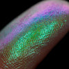 Nahaufnahme einer Fingerspitze, die in den Pastel Duochromes Loose Eyeshadow Pom Pom getaucht wurde und lila und grün glitzert.