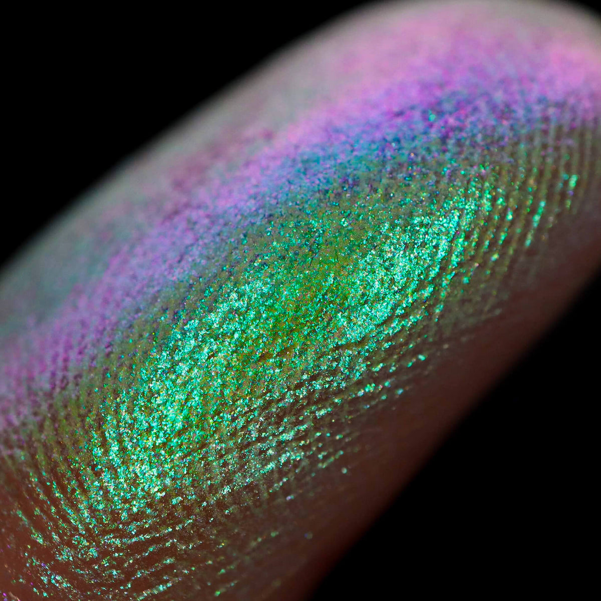 Nahaufnahme einer Fingerspitze, die in den Pastel Duochromes Loose Eyeshadow Pom Pom getaucht wurde und lila und grün glitzert.