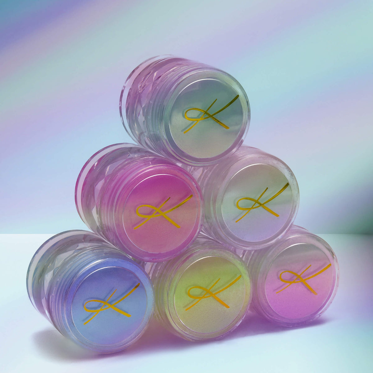 Sechs Tiegel des Pastel Duochromes Loose Eyeshadow gestapelt wie einer Pyramide vor weißem Hintergrund.