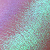 Nahaufnahme der Textur der Pressed Opal Multichrome Eyeshadow Birdsong, die rosa und türkis auf der Haut schimmert.